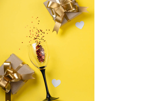 Valentine's Day background. Clinking wine glasses, various handmade gift boxes decorated with pink heart confetti on yellow background. Valentines day concept. Flat lay, top view, copy space - Fotoğraf, Görsel