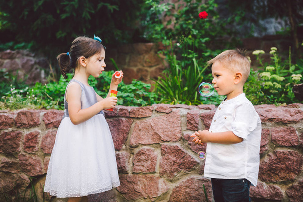Two children in the park blowing soap bubbles and having fun. Two baby Playing With Soap Bubbles. brother and sister having fun outdoors, happy childhood concept - Foto, Imagen