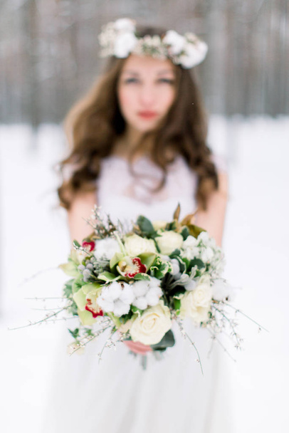 Winter wedding flower bouquet with cotton. Young and beautiful bride with the flower bouquet in winter forest. Focus on the bouquet - Fotografie, Obrázek