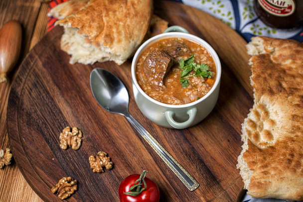 Sopa de kharcho con carne de cordero servida en un tazón de barro con pan plano de lavash
 - Foto, imagen