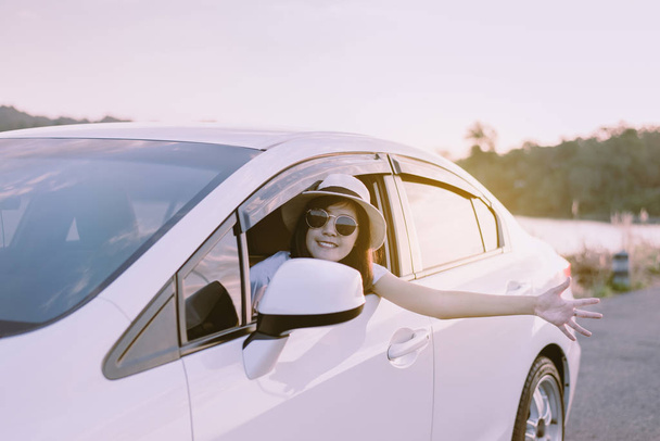 Šťastná asijská žena nosí klobouk a sluneční brýle sedí v autě se západem slunce, Relaxační čas, Pozitivní myšlení - Fotografie, Obrázek