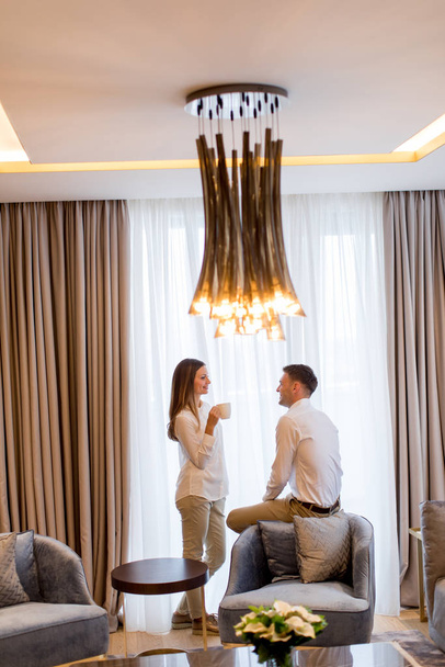 Молодая пара расслабляется и беседует с чашками кофе в роскошном номере современной квартиры
 - Фото, изображение