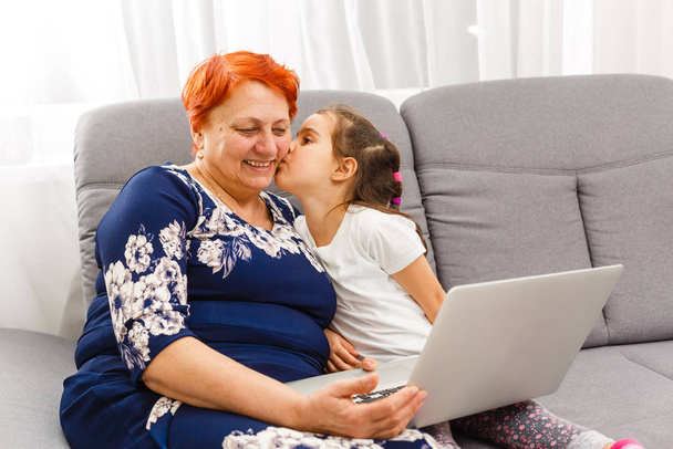 Isoäiti käyttää kannettavaa tietokonetta ja laskin kanssa tyttärentytär
 - Valokuva, kuva