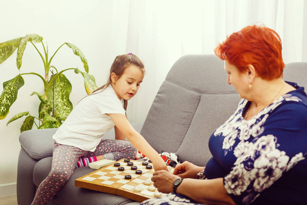 Boldog lány nagymamával ül a kanapén és sakkozik - Fotó, kép