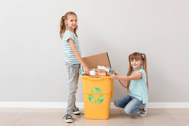 Little children and container with trash near light wall. Concept of recycling - Photo, Image