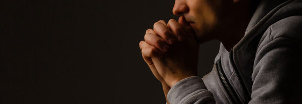 Náboženský mladý muž modlí k Bohu na tmavém pozadí, černé a - Fotografie, Obrázek