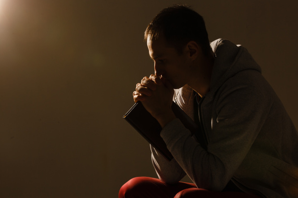 Religieuze jongeman biddend tot God op donkere achtergrond, zwart en - Foto, afbeelding