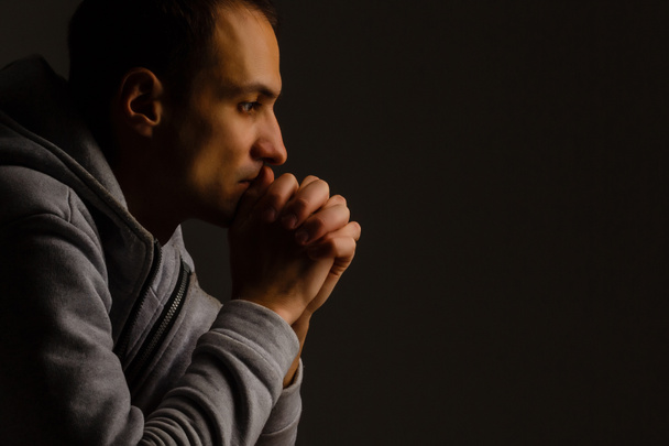 Religious young man praying to God on dark background, black and - Foto, Imagen
