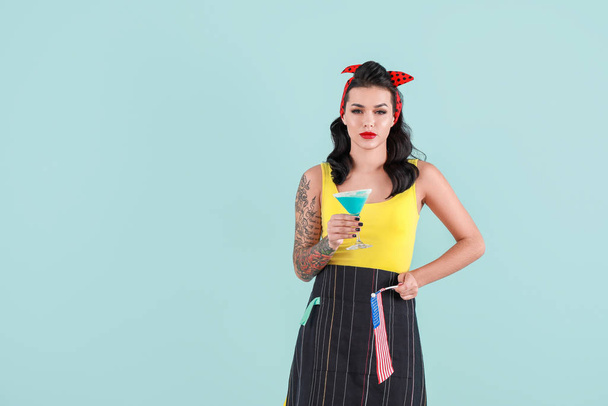 Portrait of beautiful tattooed pin-up woman with USA flag and cocktail on color background - Photo, Image