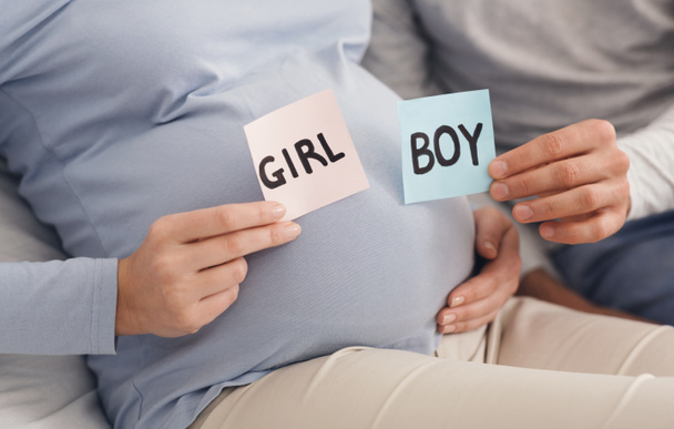 Paar houden jongen en meisje kaarten in handen in de buurt van zwangere buik - Foto, afbeelding