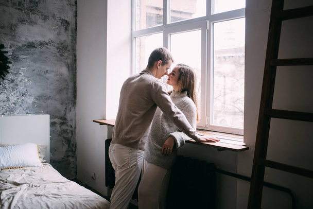 Young couple in love hug each other standing near window at home - Fotoğraf, Görsel