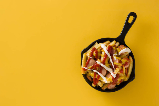 Typical Latin America Salchipapa. Sausages with fries, ketchup, mustard and mayo in iron pan and yellow background. Top view Copy space - Foto, afbeelding