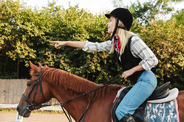 Image of woman wearing hat pointing finger while riding horse at - Fotoğraf, Görsel