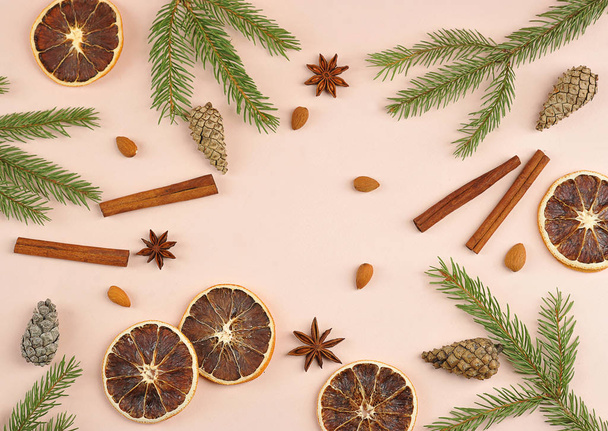 Christmas composition on a pink background.  Cinnamon, anise, almonds, cones, slices of orange, spruce branches occupy the entire space of the frame. - Foto, afbeelding