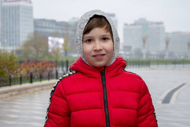 Utcai portré egy fiúról egy gettóban, körülbelül 10 éves, vidáman nevet a város toronyházainak hátterében, a folyó torkolatánál, köd a városban. Egészséges gyermekkor, jó orvoslás. - Fotó, kép