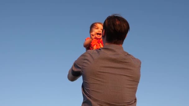 família feliz jogando à noite contra o céu. pai joga seu filho no céu azul papai brinca com uma filhinha, o bebê sorri e se alegra. Movimento lento
. - Filmagem, Vídeo
