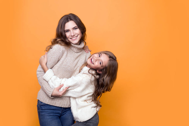 glückliche Familie. Mutter mit hübscher Tochter im Pullover, die sich auf orangefarbenem Hintergrund umarmt - Foto, Bild