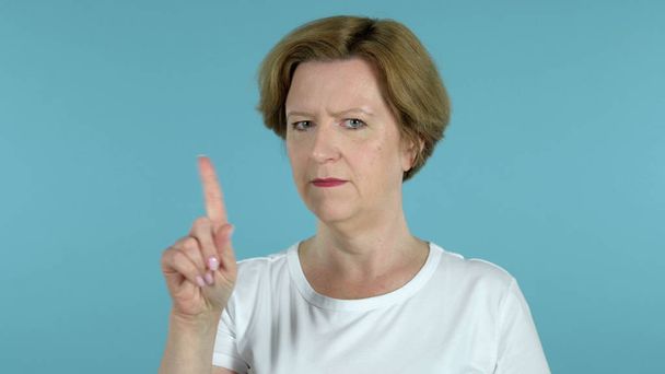 alte Frau winkt mit dem Finger ab, um sich isoliert auf blauem Hintergrund zu verweigern - Foto, Bild