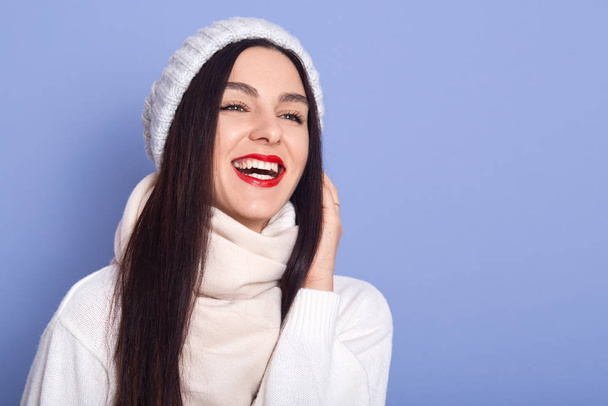 Relaxed caucasian woman wearing white warm sweater, standing and laughing in studio. Amazing girl with bright makeup expressing happiness, copy space for your advertisment or promotional text. - Foto, Bild
