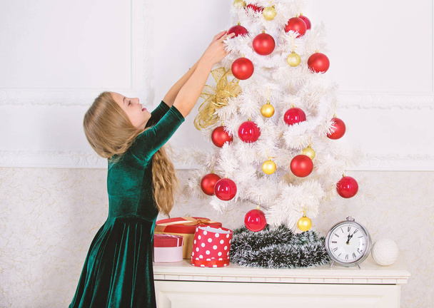 Child hang christmas ornament ball on artificial tree. Kids can brighten up christmas tree by creating their own ornaments. Girl celebrate christmas. Top christmas decorating ideas for kids room - 写真・画像