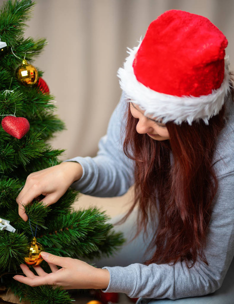 Donna felice in cappello di Babbo Natale decora l'albero di Capodanno
 - Foto, immagini