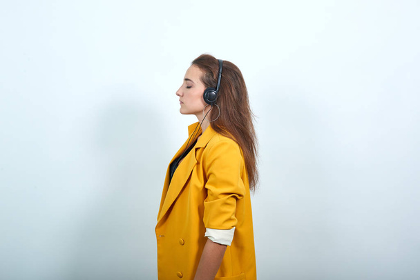 Caucasian young woman in yellow jacket having headphone, enjoying music - Photo, Image