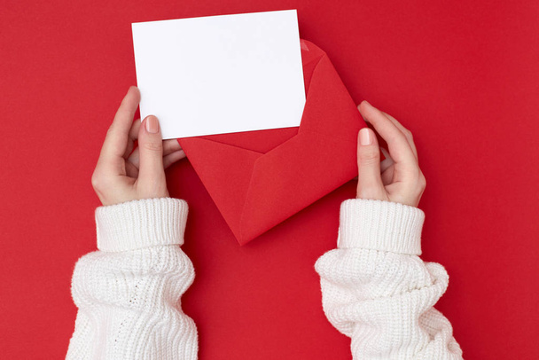 Women's hands holding an empty postcard and red envelope on the red background. Christmas concept - Фото, зображення