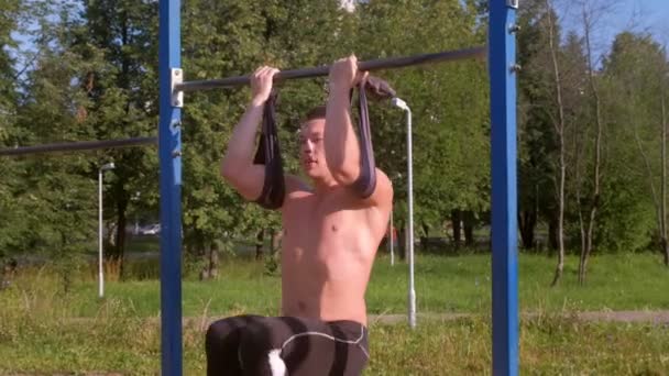 Sportsman is making abs exercise hanging on bar and lifting legs in city park. - Imágenes, Vídeo
