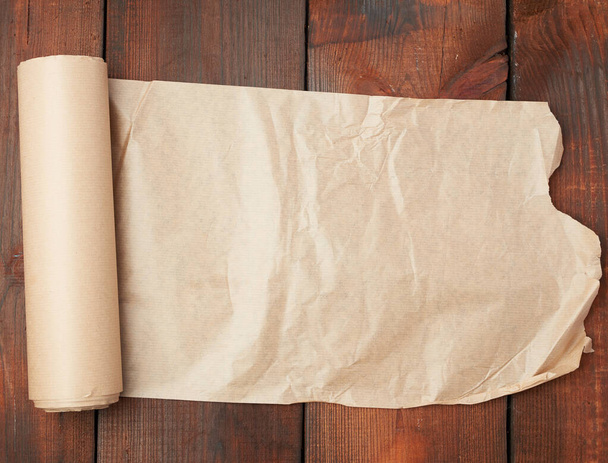 role nekrouceného hnědého papíru na dřevěném povrchu ze staré desky - Fotografie, Obrázek