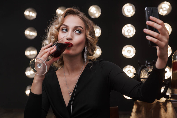Image of beautiful blonde woman using cellphone and drinking red - Фото, изображение