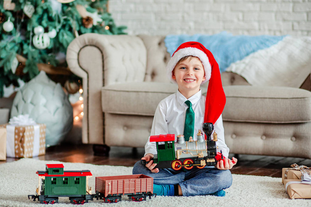 Good morning. Happy little boy with a gift, toy train, under the Christmas tree on New Year's morning. Time to fulfill wishes. - Zdjęcie, obraz