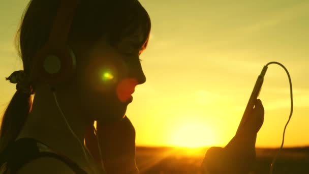 girl travels and listens to music in the warm sun. teen girl listening to music and watching the sunset. Happy girl dancing in headphones in the rays of a beautiful sunrise in the park. - Footage, Video