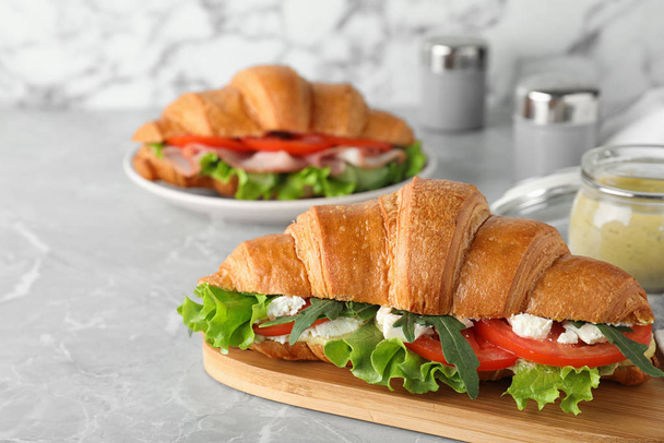 Tasty croissant sandwich with feta cheese and tomato on light grey marble table - Фото, изображение