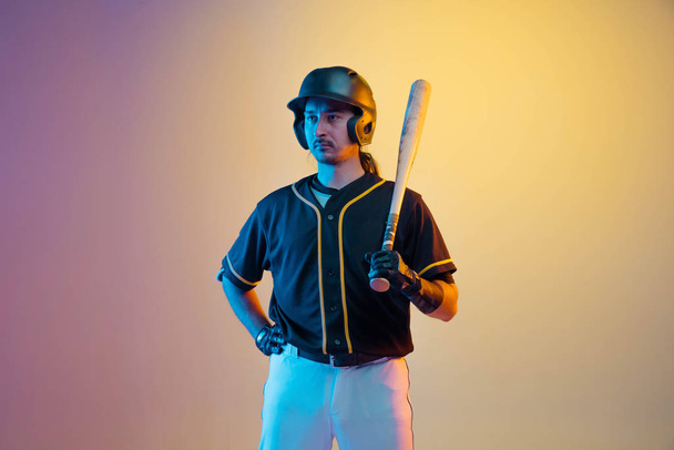 Jugador de béisbol, lanzador en uniforme negro practicando sobre fondo degradado en luz de neón
 - Foto, Imagen