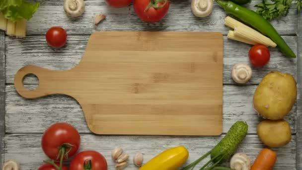 Aardappelfruit rolt langs een snijplank op een keukentafel met groenten. - Video