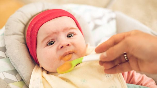 Mother feeding hungry five month old funny baby with solid food. - Fotoğraf, Görsel