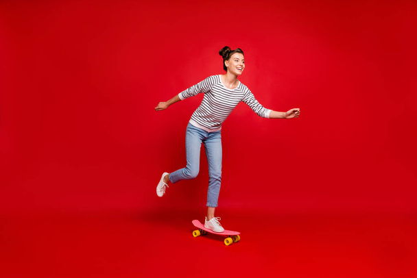 Full length profile side photo of positive cheerful girl ride have autumn free time ride her skateboard wear white outfit sneakers isolated over red color background - Φωτογραφία, εικόνα