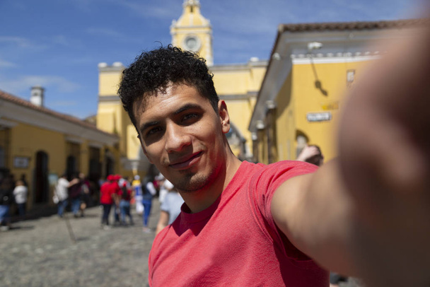 Young Latino taking a self in the city of Antigua Guatemala with the Santa Catalina Arch behind - Photo, Image