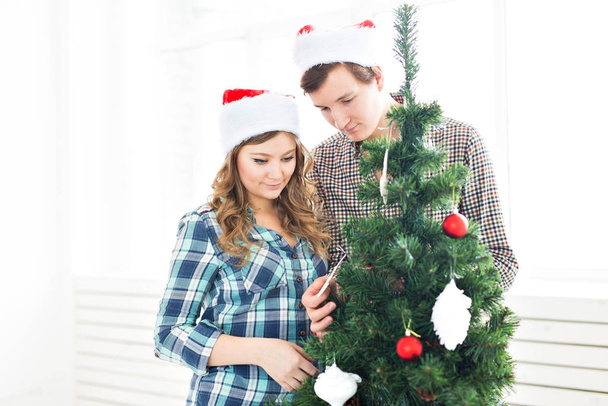 family, x-mas, winter holidays and people concept - happy young couple decorating christmas tree at home - Photo, Image