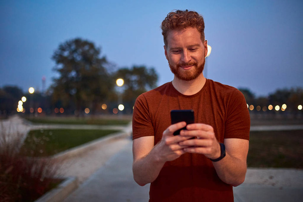 Man using cellphone in urban park at night. - Fotoğraf, Görsel
