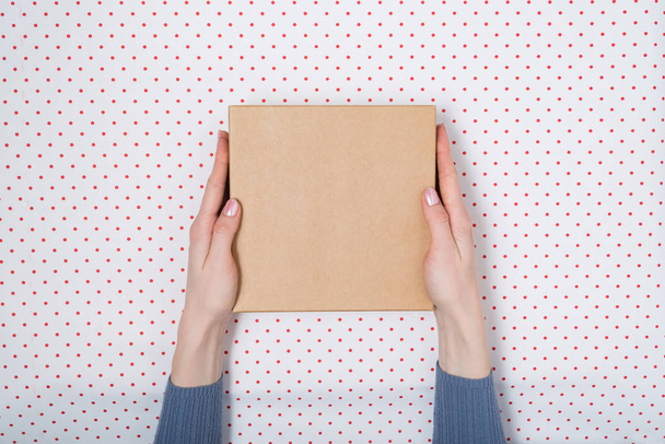 Τετράγωνο χάρτινο κουτί σε γυναικεία χέρια. Πάνω όψη, λευκό φόντο - Φωτογραφία, εικόνα