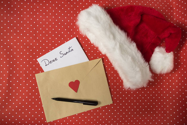 Noel Baba 'ya bir zarf içinde mektup, kalem. Noel Baba şapkası. Kırmızı benekli arka plan - Fotoğraf, Görsel