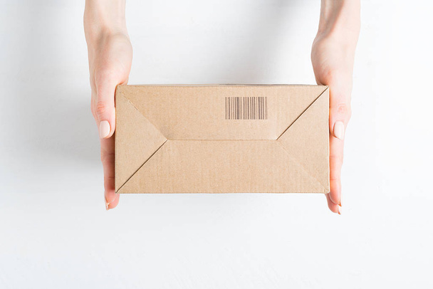 Caja de cartón rectangular con código de barras en manos femeninas. Vista superior, fondo blanco
 - Foto, Imagen