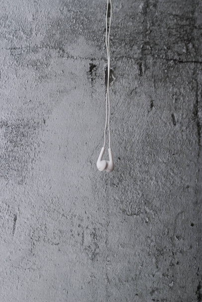 White earphone hanging on grey background - 写真・画像