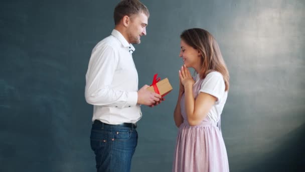 Handsome boyfriend giving present in gift box to excited young woman kissing - Filmagem, Vídeo