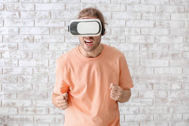 Young man with VR glasses near brick wall - Photo, Image