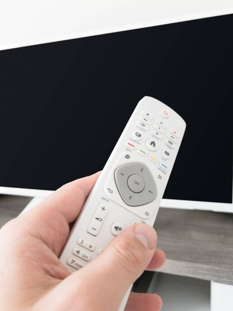 Hand holding TV remote controller with a modern television set. - Photo, Image
