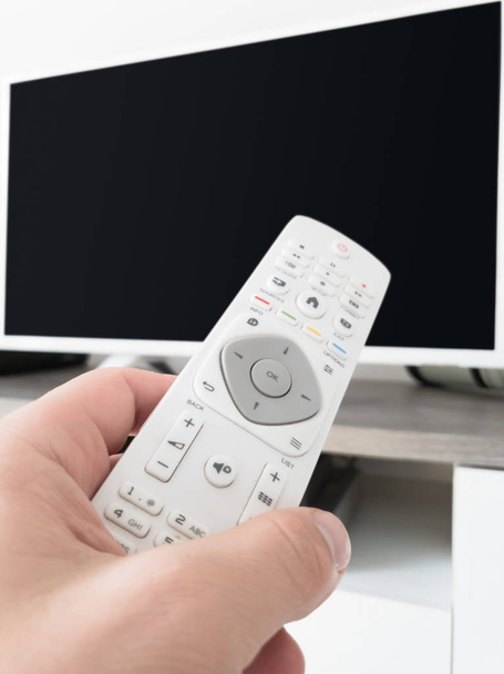 Mano que sostiene el mando a distancia de la TV con un televisor moderno
. - Foto, imagen
