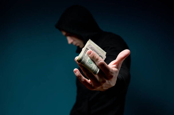 A man holds out money and hides his face. Dark silhouette with a syringe - Foto, Bild