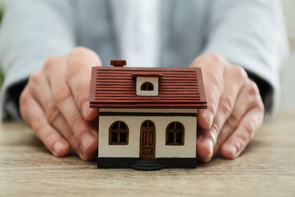 Real estate agent holding house model at wooden table, closeup - Foto, Imagen